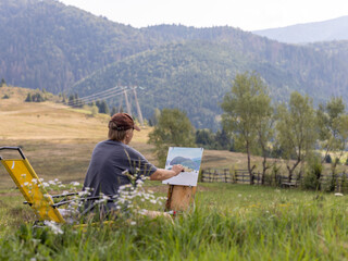 Female artist in mountainous meadow creating a painting during daylight