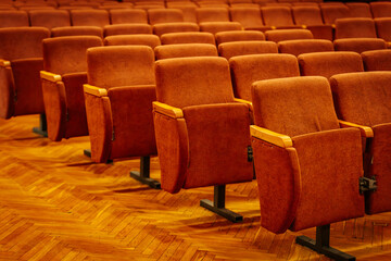 Rows of plush orange seats in an empty auditorium, set on a polished wooden floor with warm lighting and rich ambiance. Great for presentations and performances.
