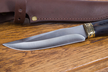 Hunting knife with leather holster on wooden background