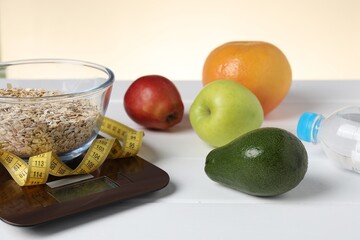 Electronic kitchen scale, measuring tape and products on white wooden table against beige background, closeup. Calories control