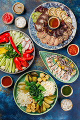 Bowls with different foods including various meat snacks, vegetable snacks made from fresh and fermented vegetables and sauces. A table with many bowls of food on it.