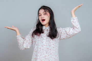 Young Asian woman with confused facial expression raising both hands as if unsure or questioning...