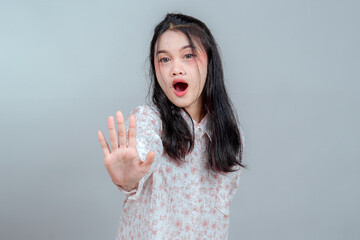 Portrait of a surprised young Asian woman with mouth open and hand raised in a stop gesture,...