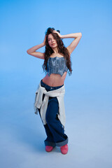 Young woman poses confidently in stylish outfit against blue backdrop