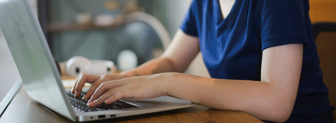 A hand Asian Student typing report and working on laptop. Beautiful young freelancer writing blog and internet work online at home office.- Technology concept banner image.