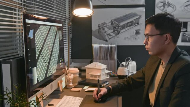 Side shot of serious young male Biracial engineer drawing on graphic tablet, designing enhanced digital solar power system model and looking at computer monitor in office, sustainable technology