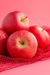 Fresh red apples in a red mesh bag on a pink background.