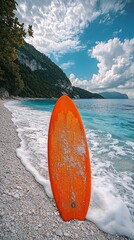 Orange surfboard on pebble beach, coastal mountains background, summer day