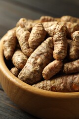 Tumeric rhizomes in bowl on wooden table, closeup