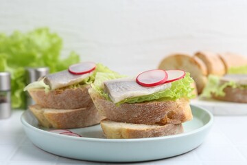 Tasty sandwiches with herring, radish and lettuce on white table, closeup