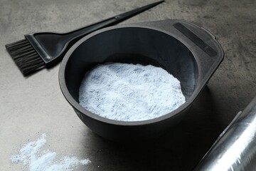 Bowl with hair bleaching powder, foil and brush on grey table, closeup