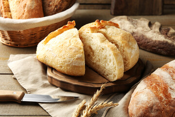 Different loaves of fresh bread, knife and spikes on wooden table, closeup