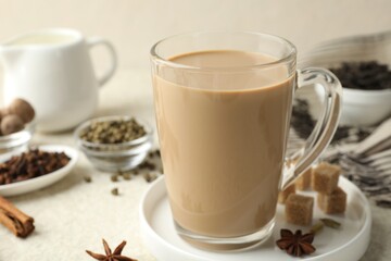 Aromatic Masala tea in glass cup, spices and brown sugar on white textured table, closeup