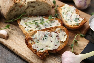 Tasty bread with garlic, herbs and oil on wooden table, closeup