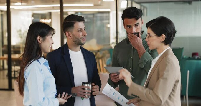 Positive diverse office coworkers chatting in lobby area on work break, holding gadget, document, mug of drink, talking, chatting, meeting briefly for corporate networking