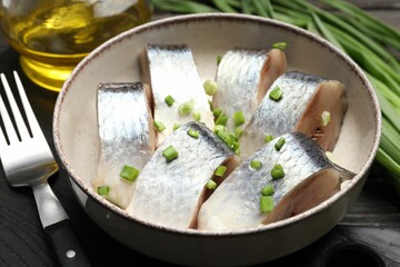 Pieces of delicious herring with green onions served on black wooden table, closeup