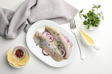 Tasty herring fillets with onions and parsley served on white table, flat lay