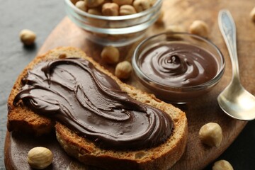 Slice of bread with chocolate spread and hazelnuts on table, closeup