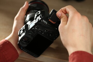 Man inserting SD memory card into photo camera at table, closeup
