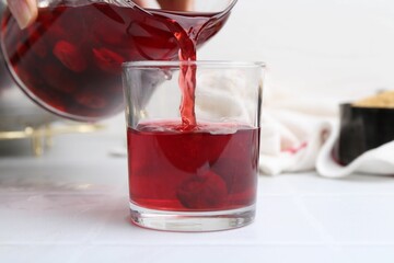 Pouring tasty cherry compot into glass on white tiled table, closeup