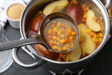 Taking tasty compot with ladle from pot on grey wooden table, closeup