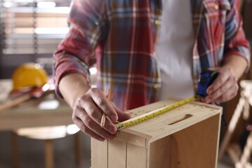 Man measuring wooden shelf with tape and pencil indoors, closeup