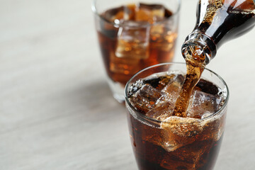 Pouring refreshing cola from bottle into glass at light grey table, closeup. Space for text