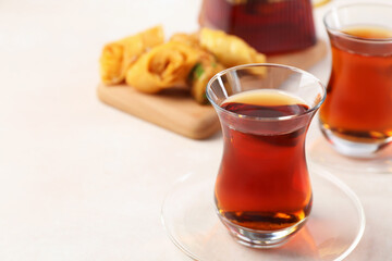 Traditional Turkish tea in glass cups, teapot and fresh baklava on white table, closeup. Space for...