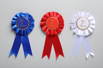 Colorful award ribbons on light grey background, flat lay