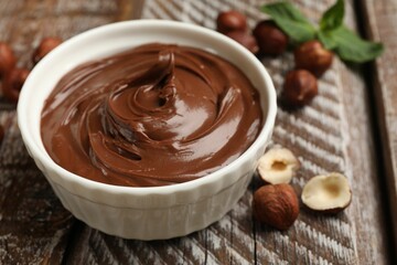Chocolate hazelnut spread in bowl, nuts and mint on wooden table, closeup