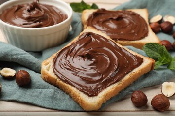 Toasts with chocolate hazelnut spread, nuts and mint on wooden table, closeup