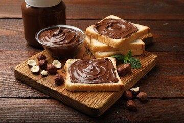 Toasts with chocolate hazelnut spread, nuts and mint on wooden table, closeup