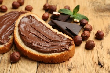 Toasts with tasty hazelnut spread, chocolate pieces and nuts on wooden table, closeup