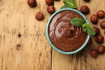 Tasty chocolate hazelnut spread with mint and nuts on wooden table, flat lay. Space for text