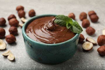 Tasty chocolate hazelnut spread with mint and nuts on grey table, closeup