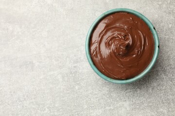 Tasty chocolate spread in bowl on grey table, top view. Space for text