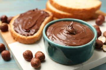 Toast with tasty chocolate hazelnut spread and nuts on blue table, closeup
