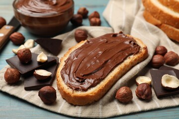 Toast with tasty hazelnut spread, chocolate pieces and nuts on blue wooden table, closeup