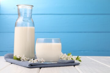 Fresh milk and blossoms on white wooden table against light blue background, closeup. Space for text