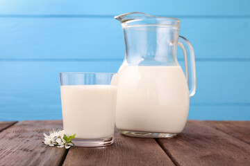 Fresh milk and blossoms on wooden table against light blue background, closeup