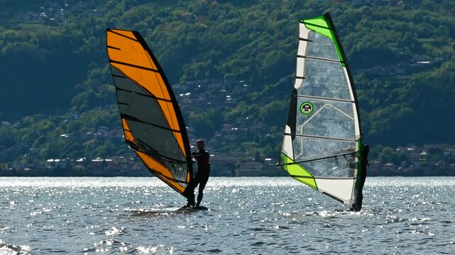 windsurfers learn at lake como during a sunny and windy day among the waves with the mountains in the background