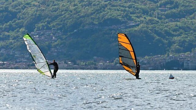 windsurfers learn at lake como during a sunny and windy day among the waves with the mountains in the background