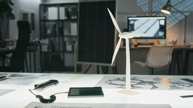 No people close-up of white wind turbine model on drafting table among sketches in renewable and sustainable technology office with solar panel prototype in background, copy space