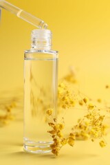 Dripping serum from pipette into bottle and gypsophila flowers on yellow background, closeup