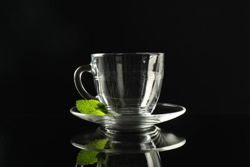 Glass cup, saucer and mint on dark mirror table
