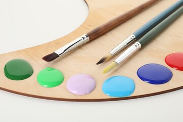 Wooden palette with paints and brushes on white background, closeup