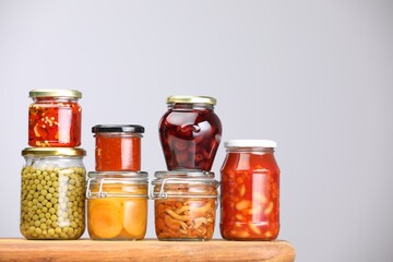 Many jars with different pickled products on wooden board against light grey background