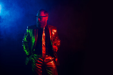 Fototapeta premium Stylish man in glossy neon suit with beard and glasses against dark background