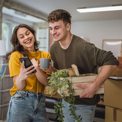adult couple move to a new house use cellphone around cardboard boxes