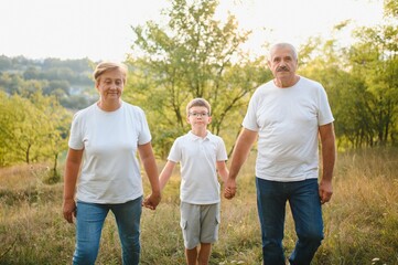 Grandson, grandfather and grandmother sitting on grass having fun outdoors in park at sunset